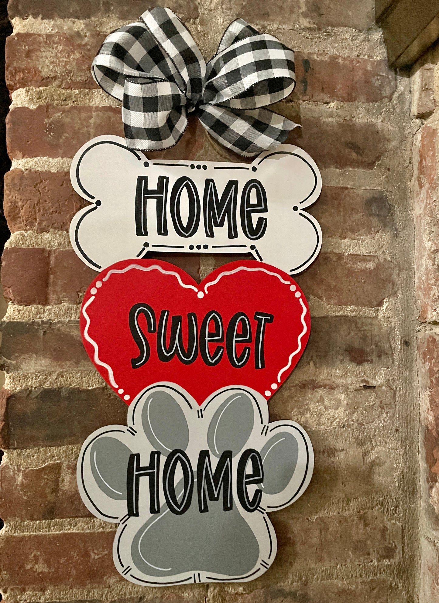 Wooden door hanger that says "Home Sweet Home" Over a bone, heart, and paw design. The door hanger has a big black & white bow on top.