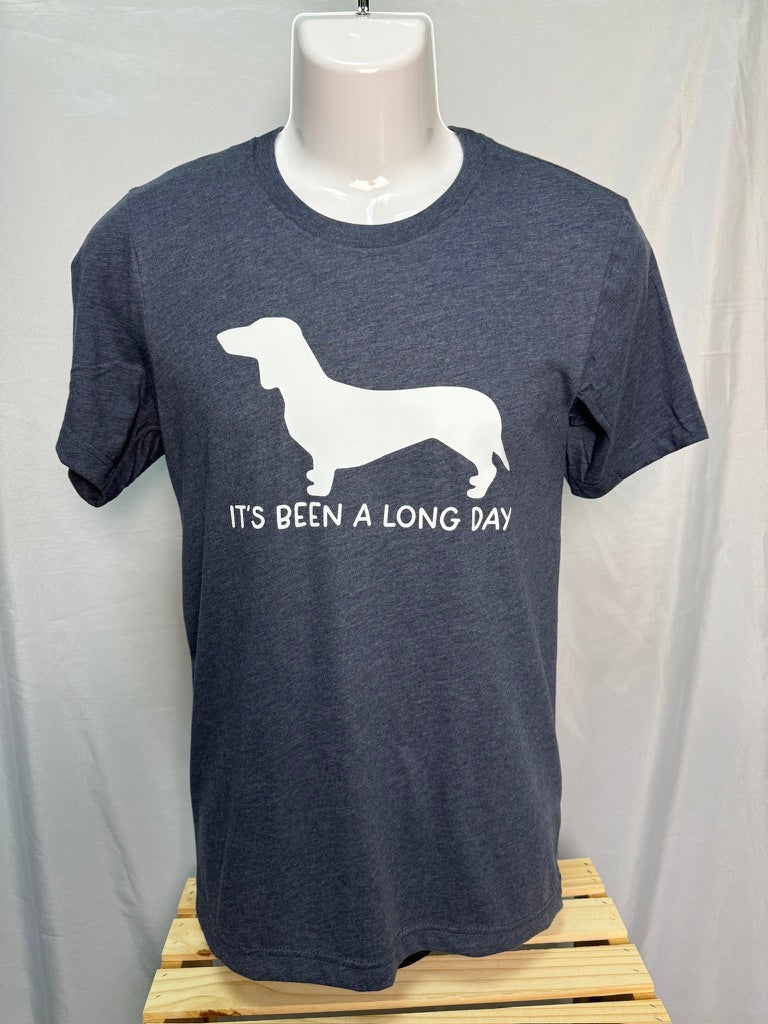 A dark gray shirt with a picture of a white wiener dog silhouette with the text "It's been a long day" in white underneath