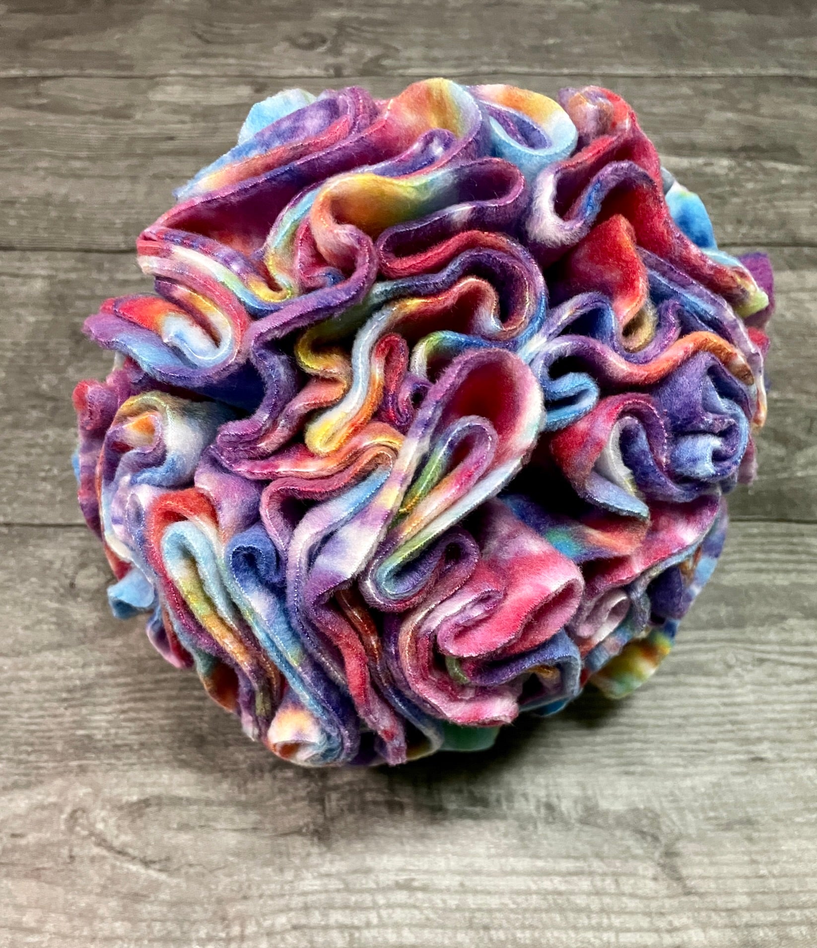a multi color snuffle ball dog toy resting on a wood table